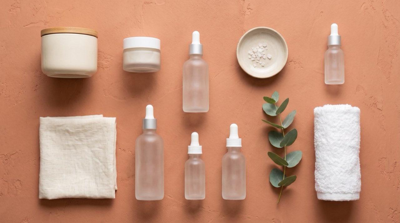 Frosted serum bottles, a folded towel and a sprig of eucalyptus laid out on terracotta plaster