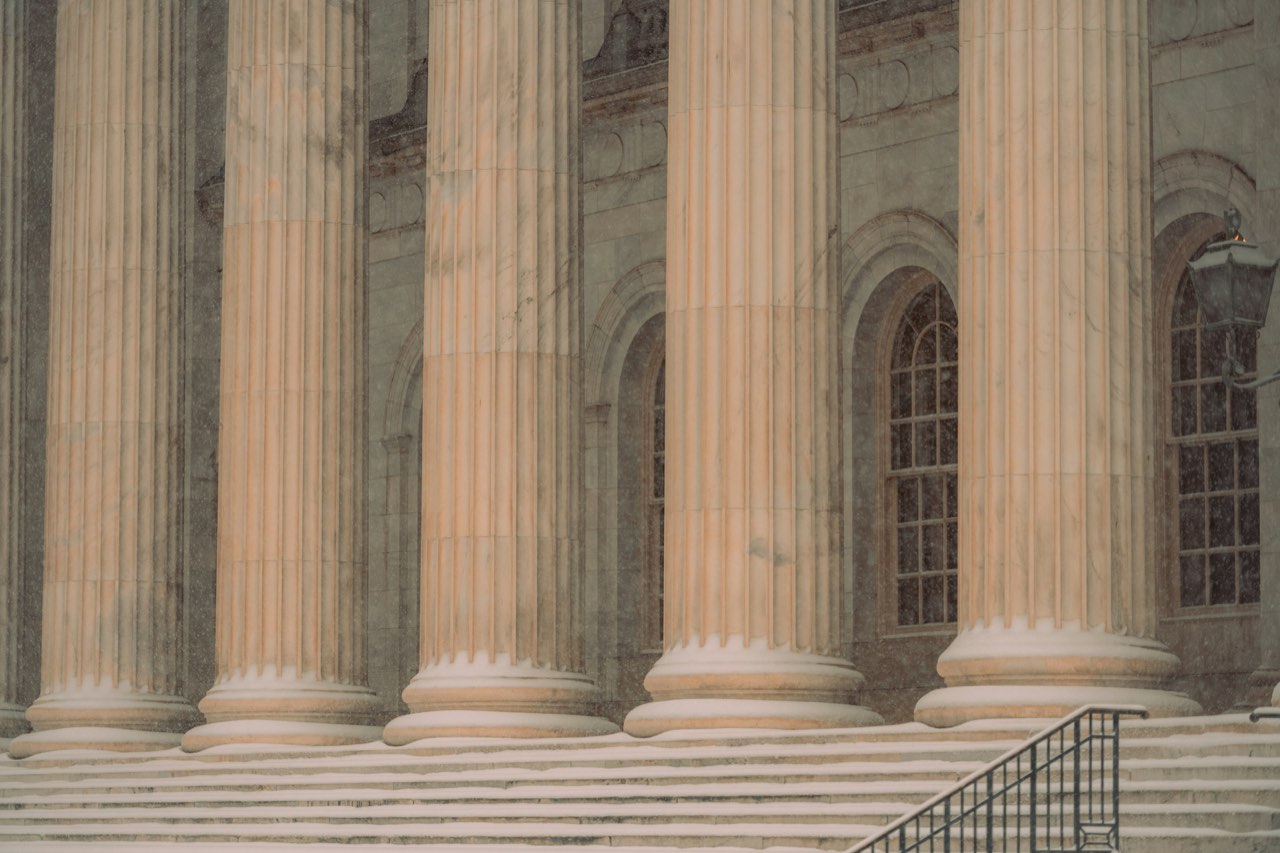 Stone columns and steps of a courthouse in falling snow, a lamp lit at the door
