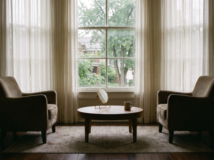 Two armchairs and a small mirror by a tall window