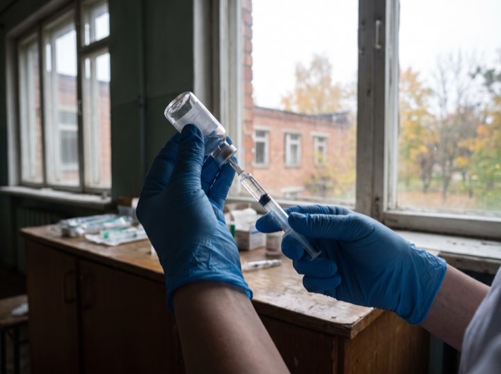 Gloved hands drawing up a syringe by a window
