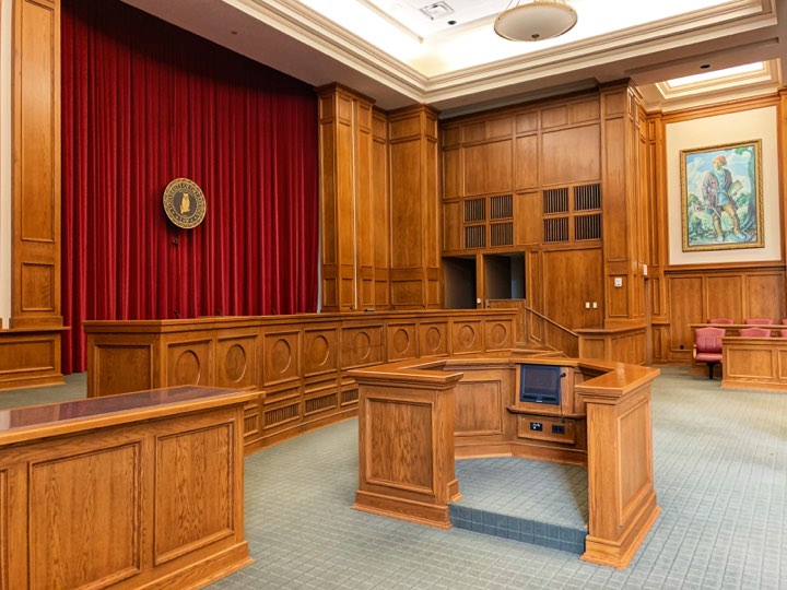 An empty courtroom in wood panelling with a red curtain behind the bench