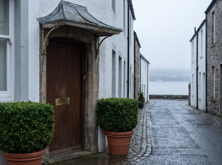 The private entrance, a stone doorway between two clipped shrubs on a quiet street