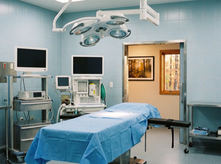 The operating suite: a draped table under twin surgical lights, monitors and anaesthesia equipment along the wall